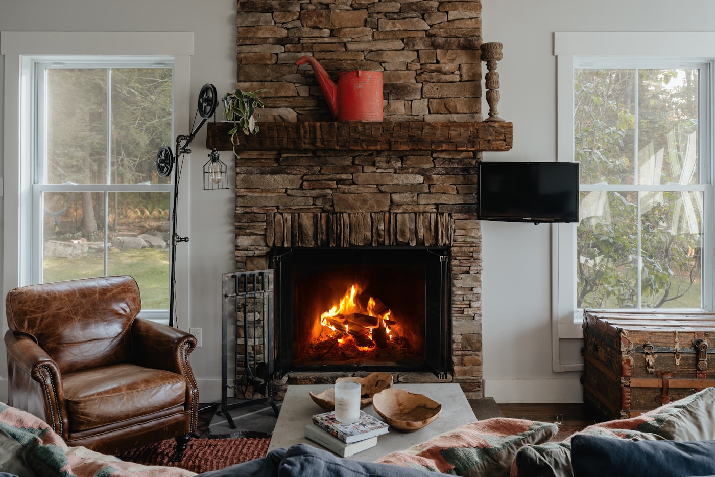 A lit stone fireplace with a timber mantel in a living room.