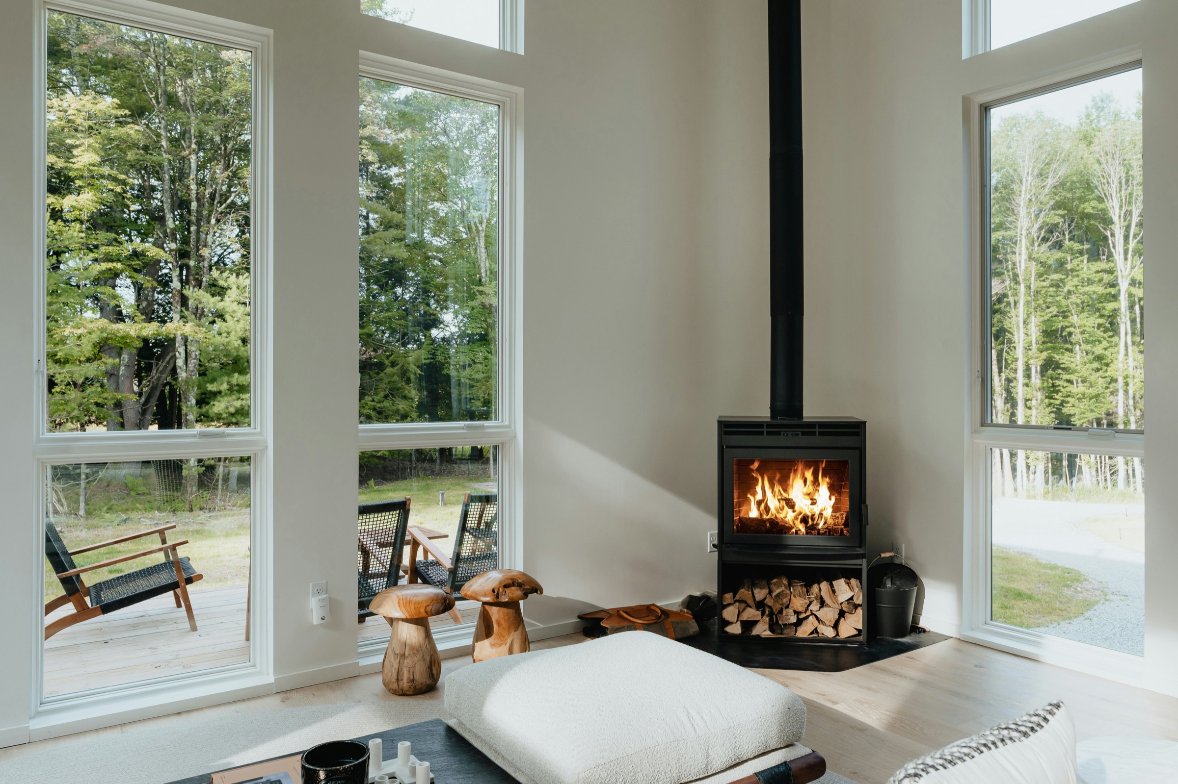 A freestanding wood stove burning in a bright room with tall windows.